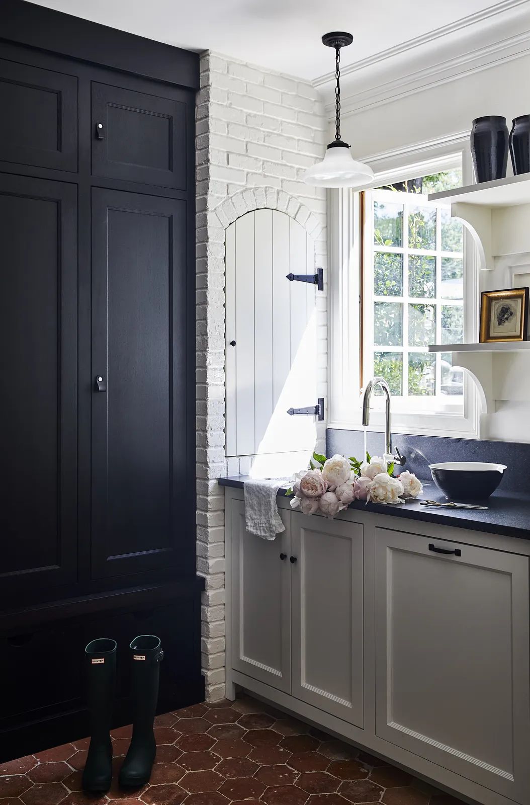 Kitchen with dark wood cabinetry, white brick wall, sink, countertop, bowl, vases, and green boots