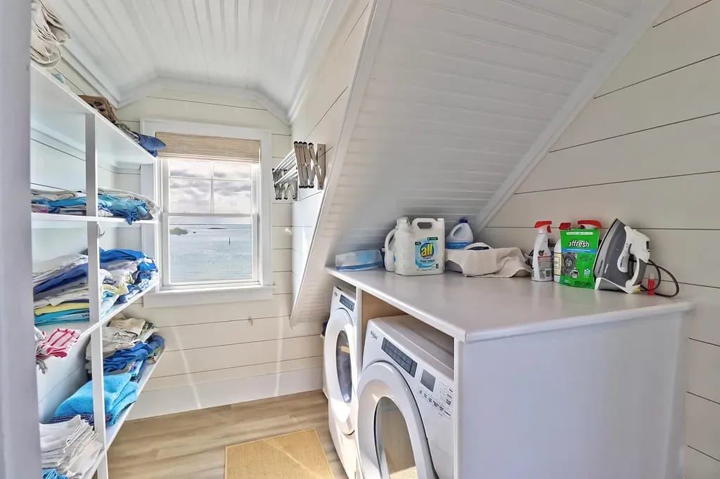 Laundry room with white shelves, washing machines, countertop, and a window with an outside view.