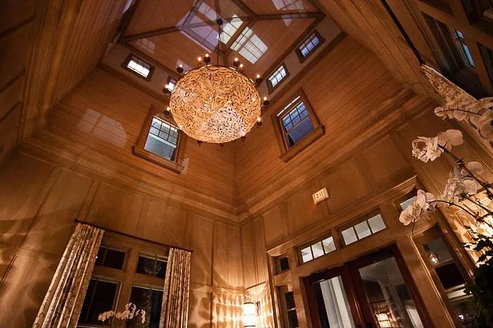 Foyer with chandelier, high ceilings, wall paneling, large windows, double doors, and white orchids.