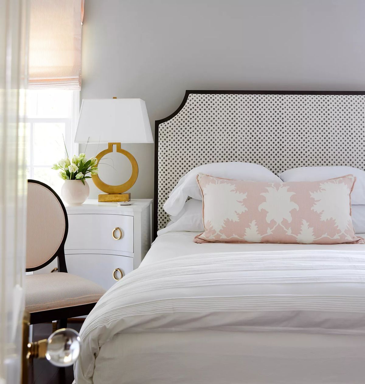 Bedroom with patterned headboard, white bedding, nightstand, table lamp, and chair in the corner.