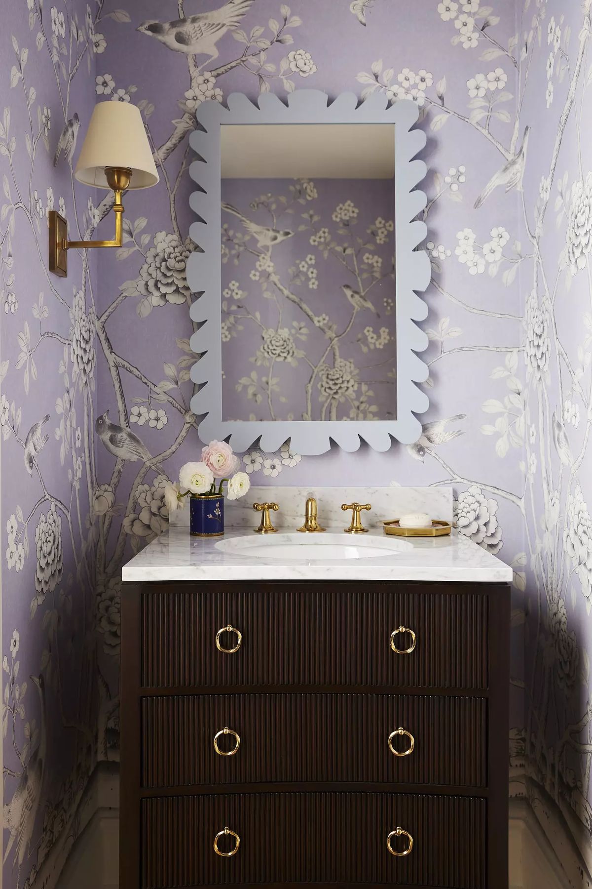 Powder room with dark wood vanity, marble countertop, blue mirror, purple floral wallpaper, and wall sconce.