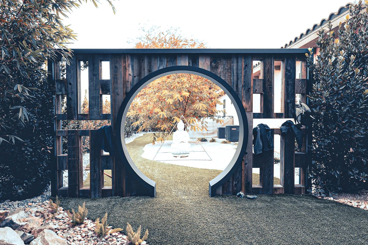 Garden with circular wooden gate, stone pathway, artificial grass, and white sculpture.