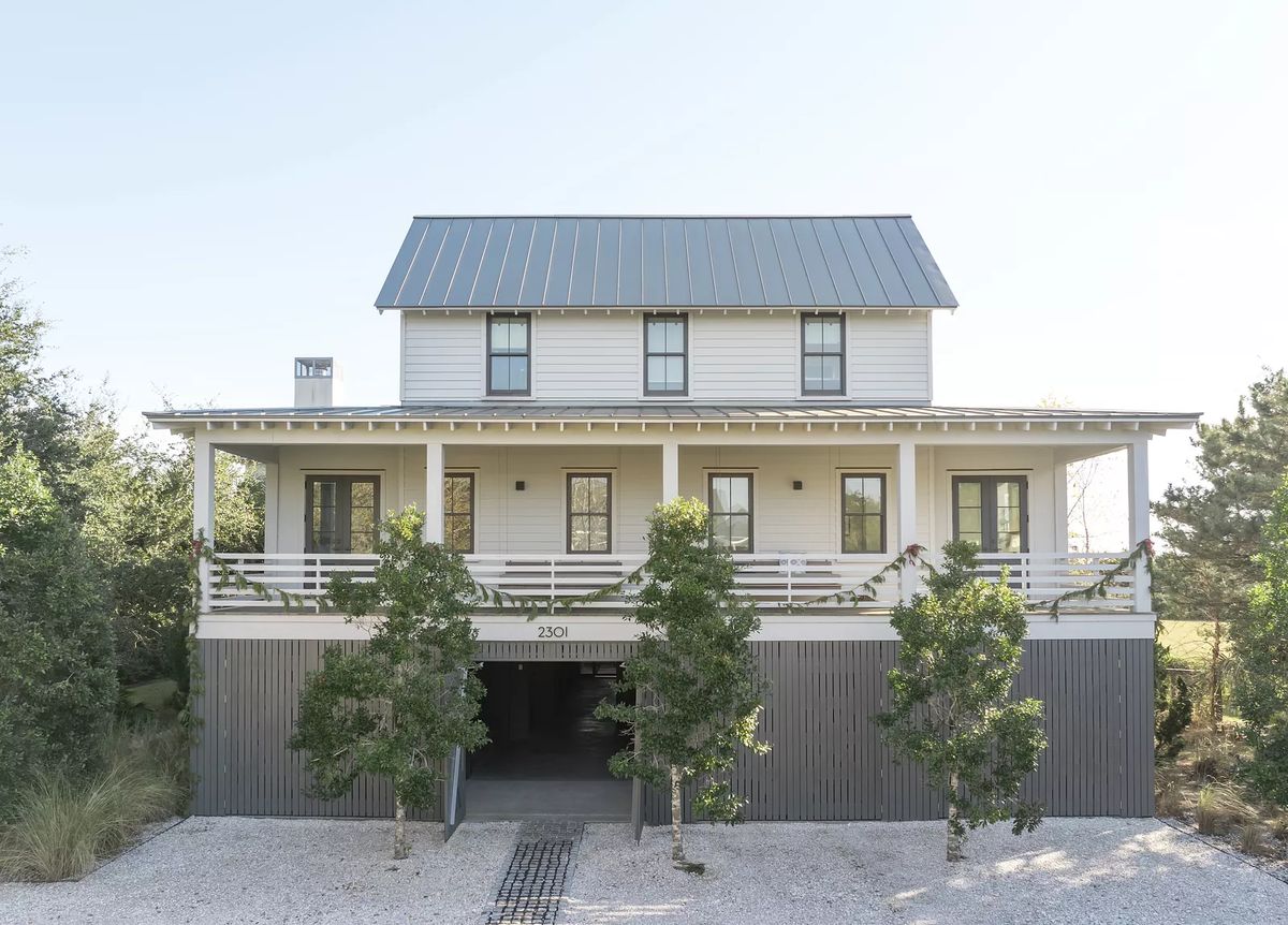 Two-story house with metal roof, white walls, front porch, and gravel driveway.