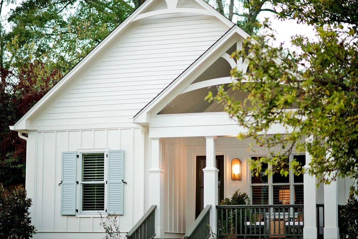 House exterior with white siding, gabled roof, front porch, blue shutters, and surrounding plants.