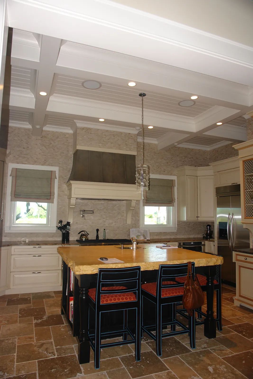 Kitchen with large island, bar stools, cabinetry, stone walls, and stainless steel appliances.