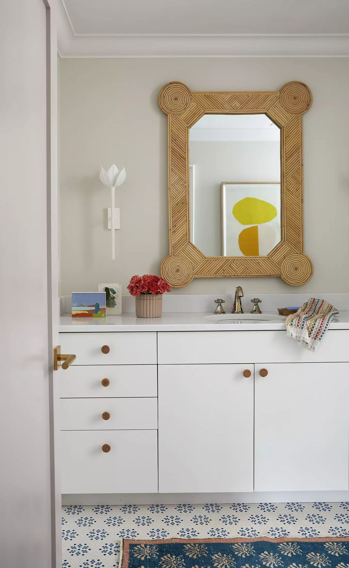 Bathroom with white vanity, woven mirror, flower vase, and patterned floor tile
