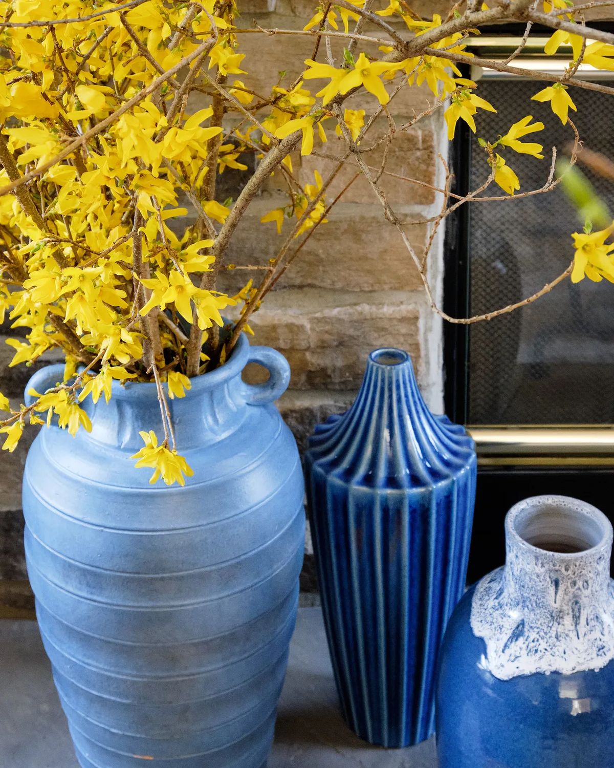 Decorative arrangement of ceramic vases with yellow flowers near a stone fireplace.