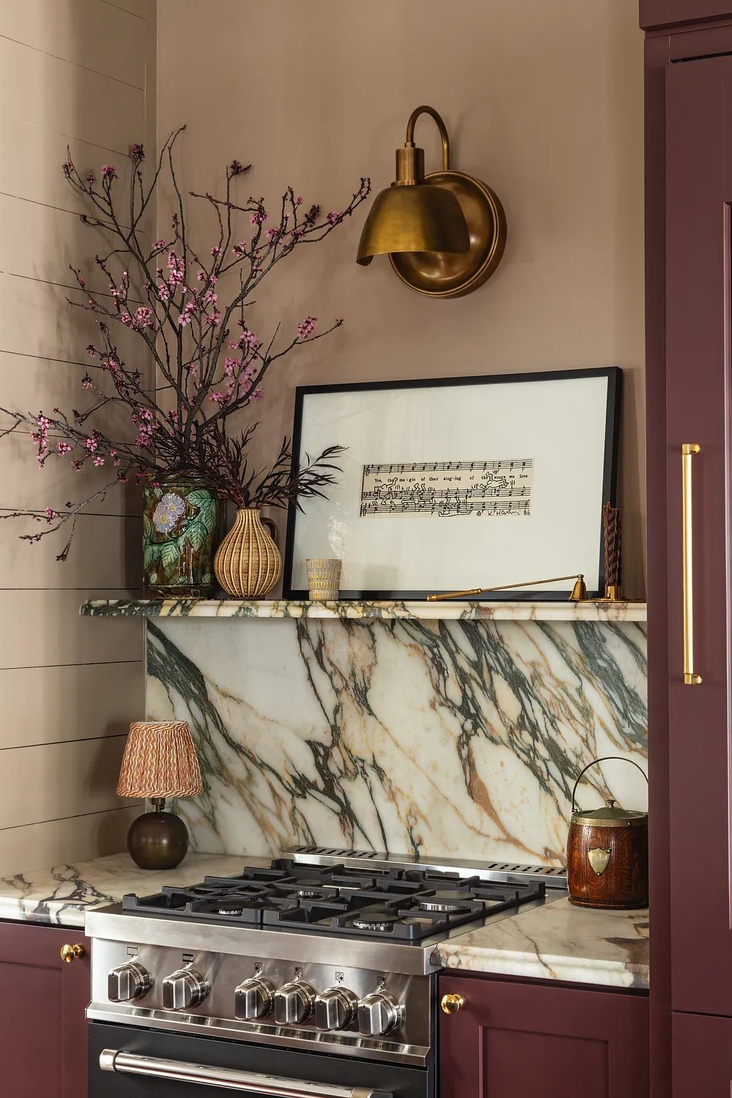 Kitchen corner with gas stove, marble backsplash, dark cabinetry, decorative shelf, and flowering branch.