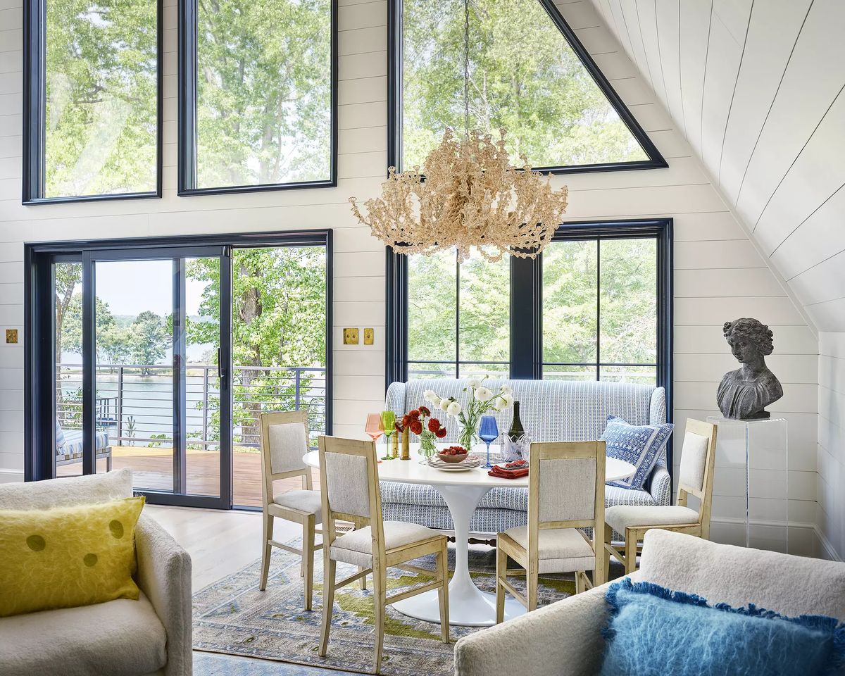 Dining room with round table, wooden chairs, blue sofa, large chandelier, and shiplap walls.