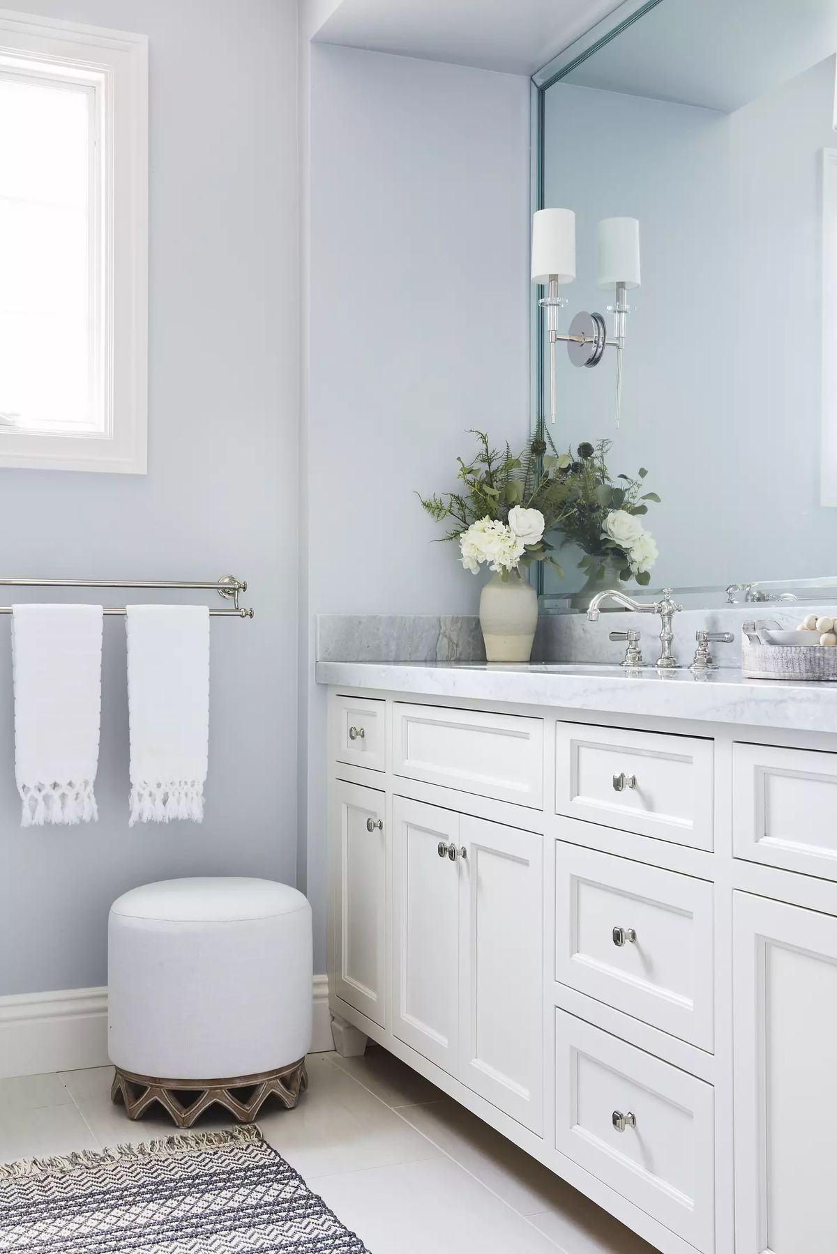 Bathroom with white vanity, marble countertop, round stool, and light blue walls with floral decor.