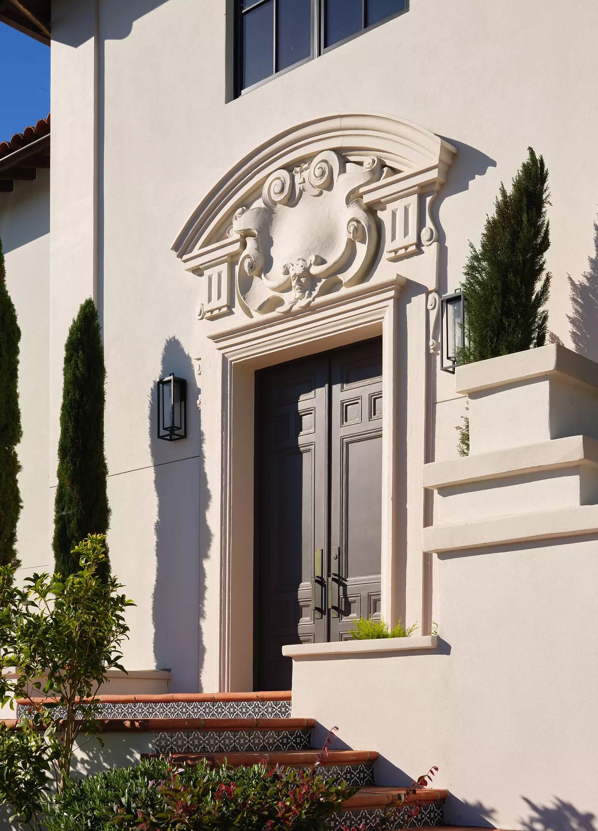 Exterior front with ornate double door, molding, cypress trees, staircase, and black wall sconces.