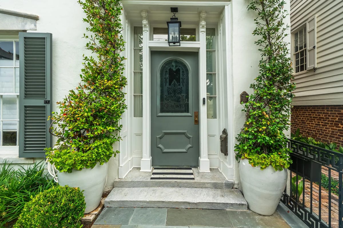Exterior front entrance with gray door, potted plants, lantern, and stone pathway.
