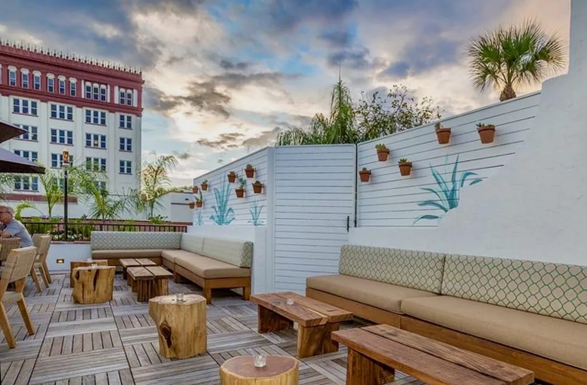 Patio with wooden tables, built-in benches, potted plants on a fence, and palm trees.