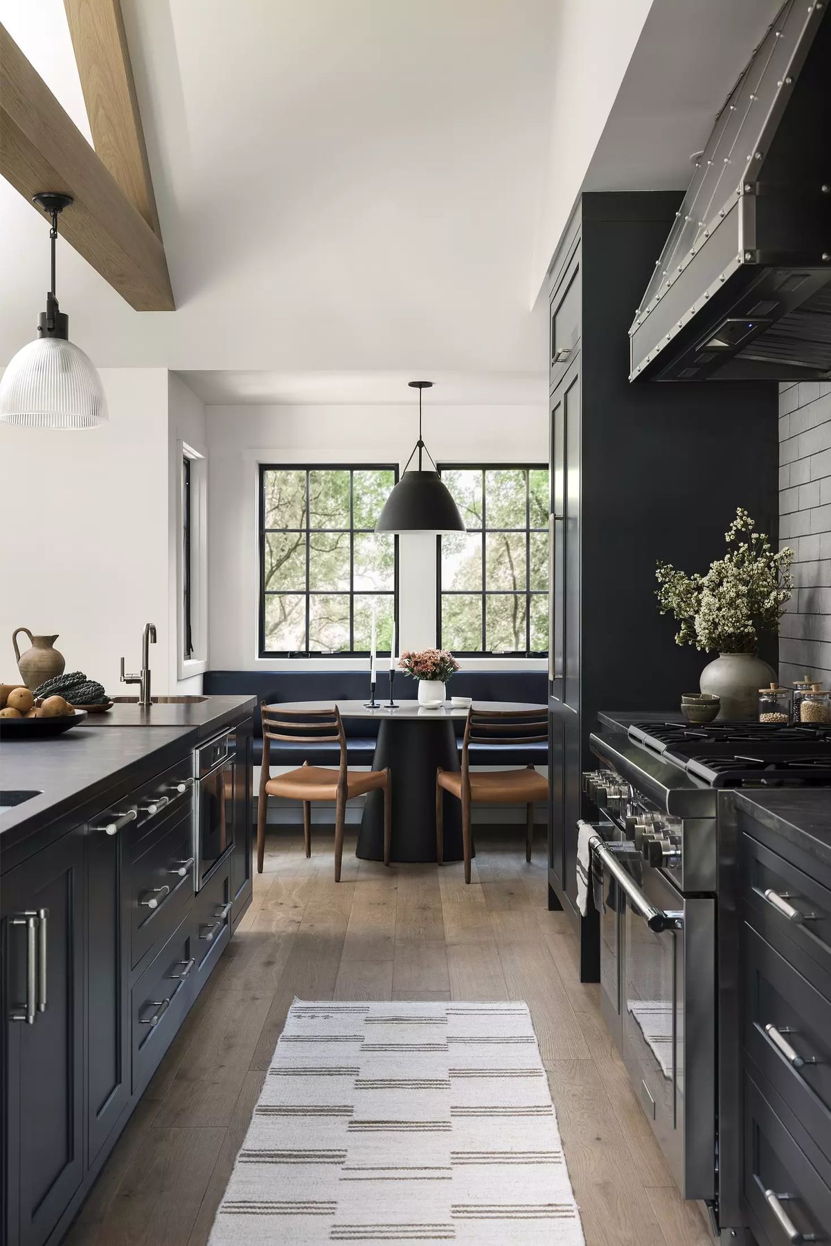 Kitchen with dark cabinetry, stainless steel appliances, large window, dining nook, and striped rug