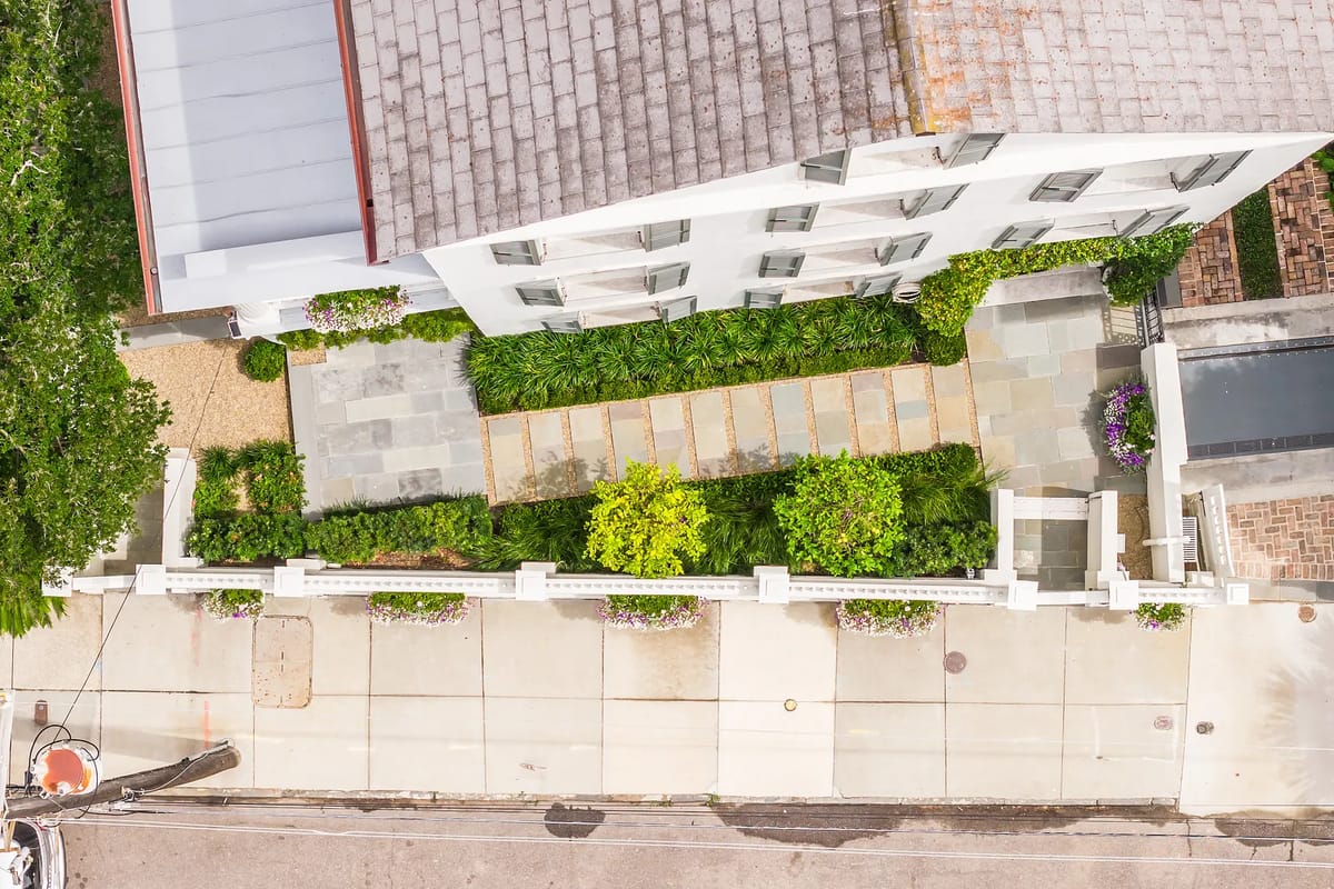 Aerial view of a garden with stone pathways, green plants, and white fence with flower pots.