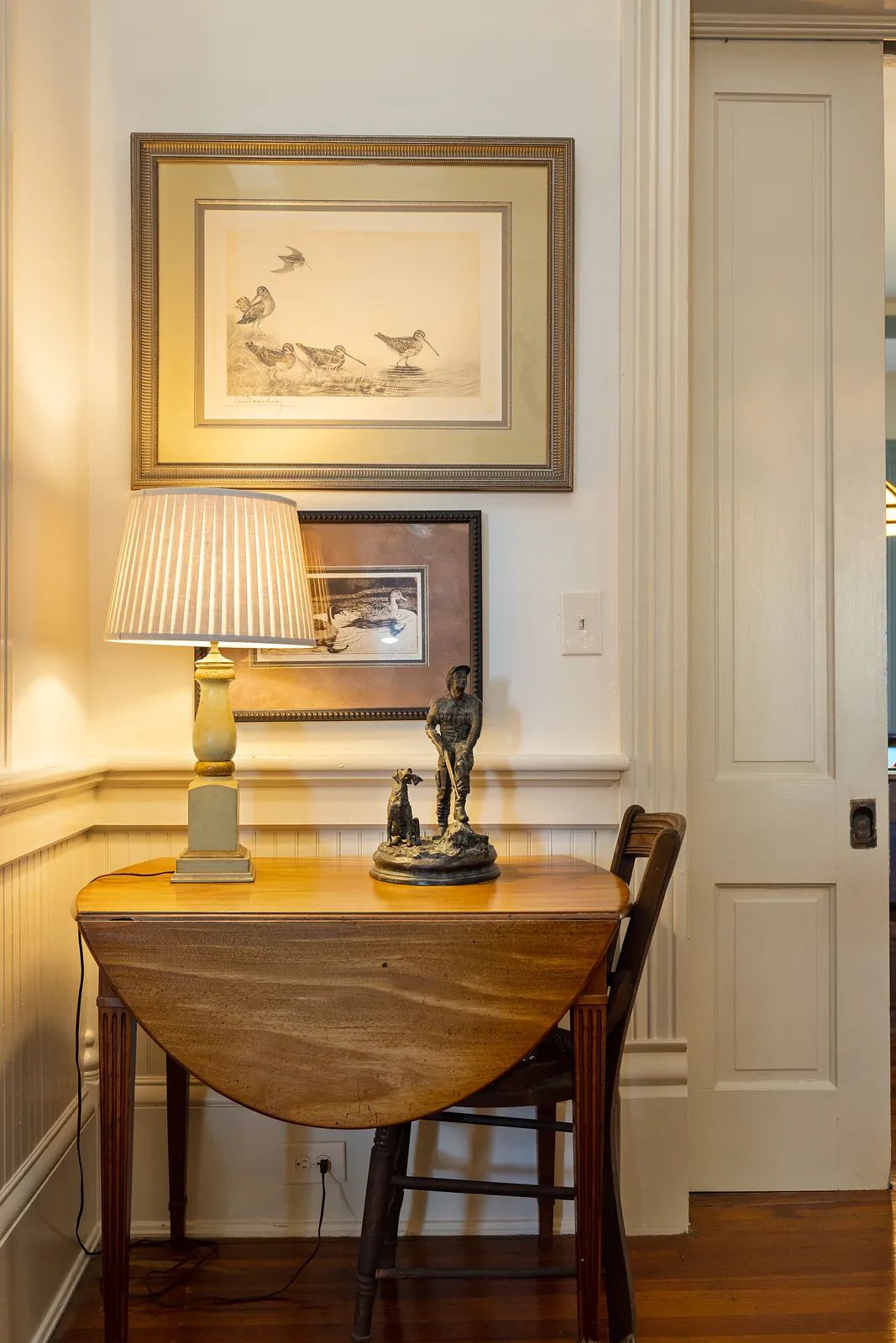 Small area with drop-leaf table, chair, sculptures, artwork, and paneled walls
