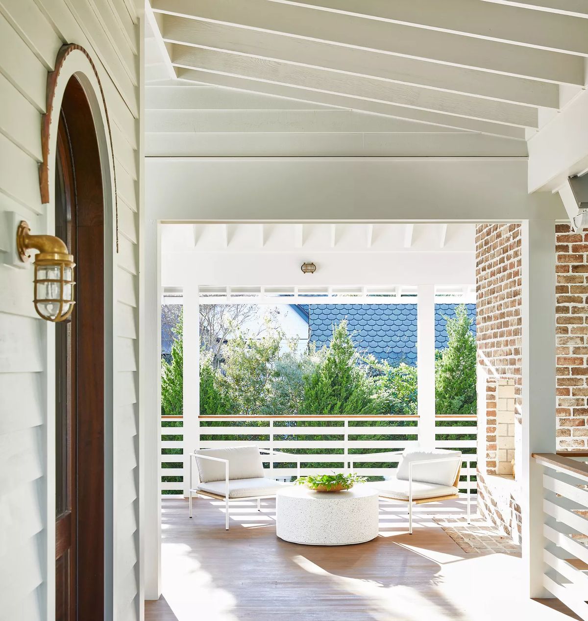 Patio with round table, two armchairs, wood flooring, and open view of greenery.