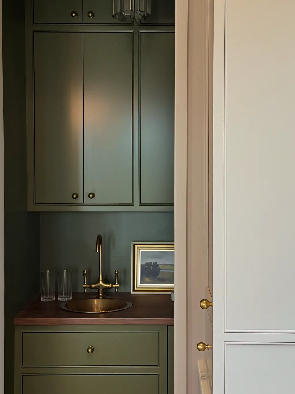 Powder room with olive green cabinetry, wooden countertop, round sink, and framed artwork.