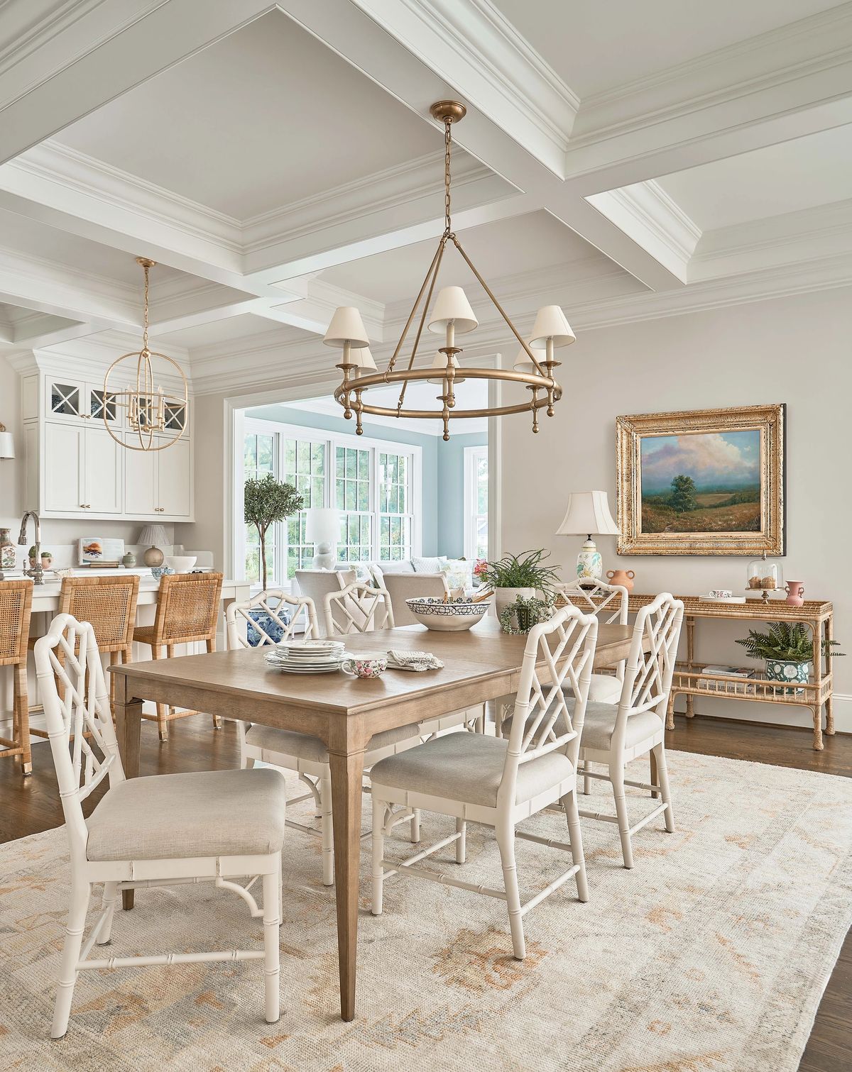 Dining room with wooden table, white lattice chairs, area rug, chandelier, and large windows.