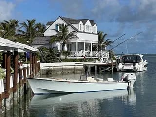 Exterior view of a white two-story house with a gray roof, docked boat, and palm trees.