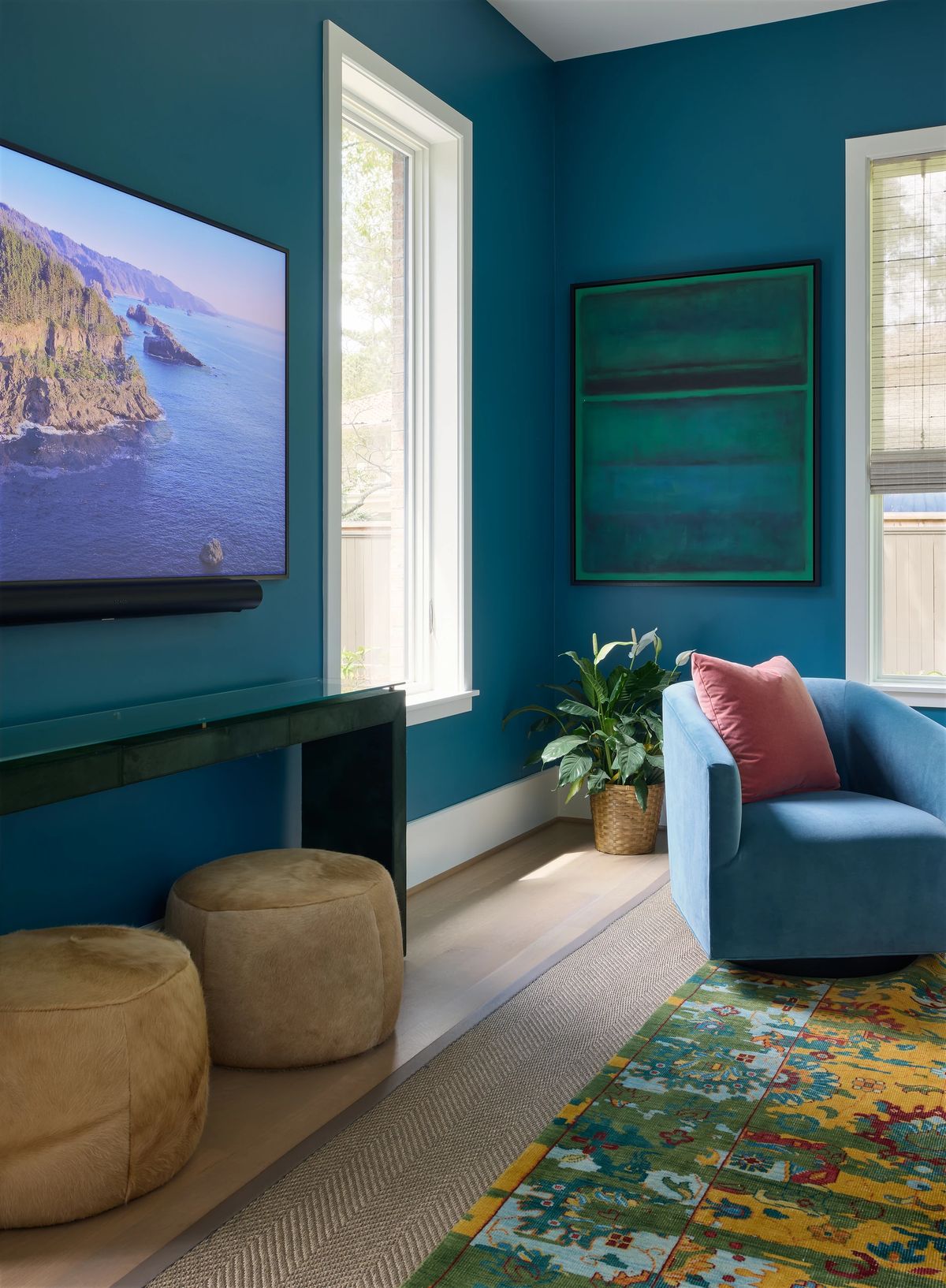 Living room with blue accent wall, mounted TV, console table, ottomans, armchair, area rug, and potted plant.