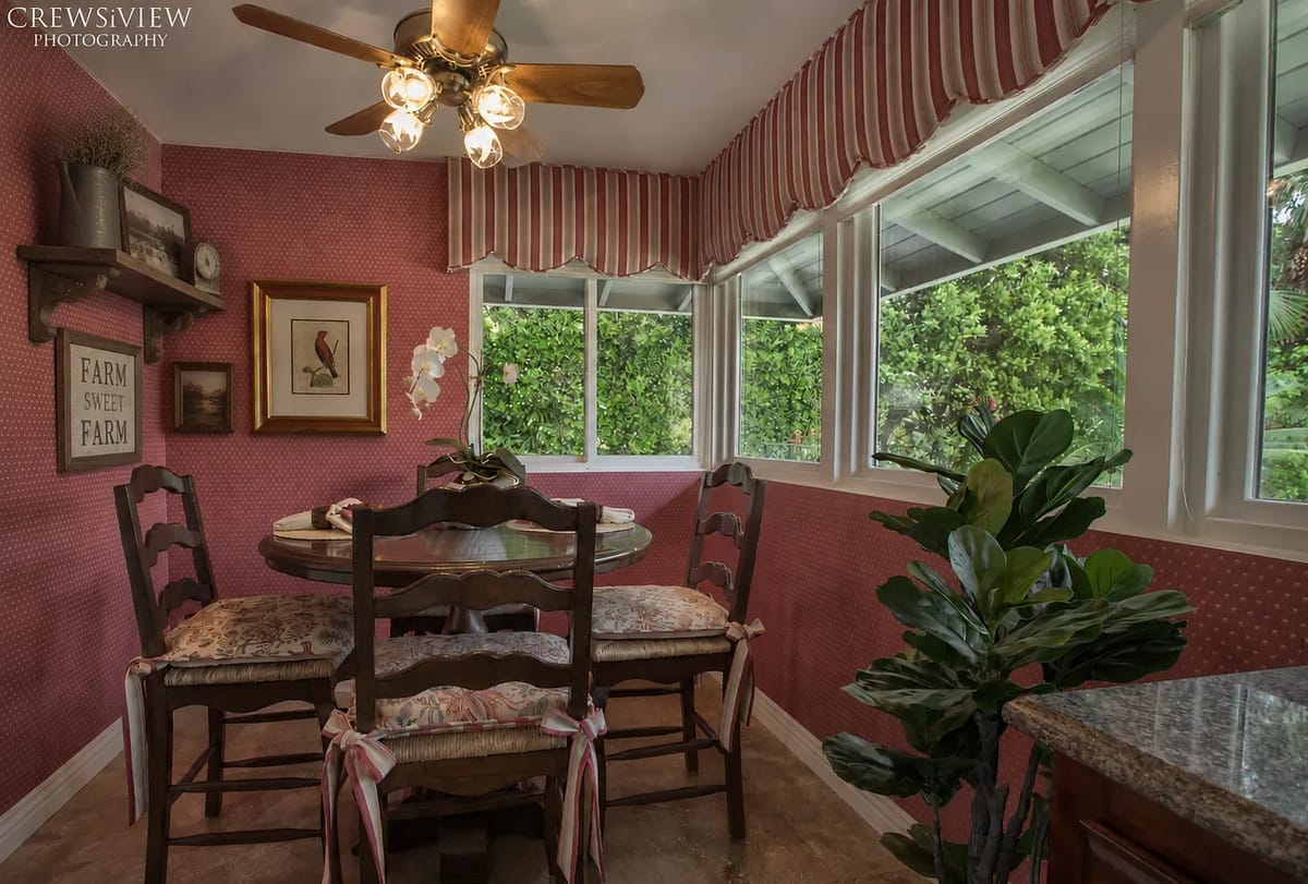 Dining room with round table, wooden chairs, pink striped walls, and a ceiling fan.
