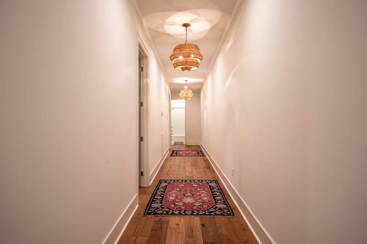 Hallway with hardwood flooring, area rugs, two woven light fixtures, and white walls.