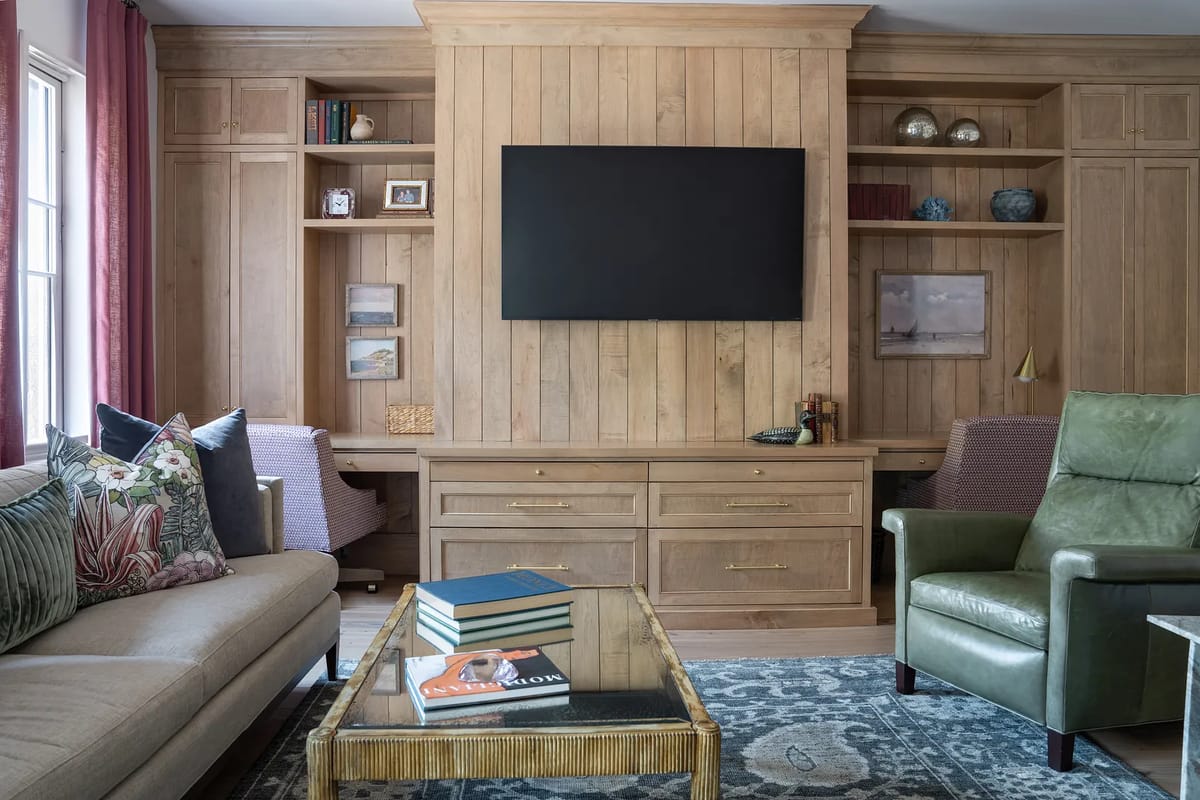 Living room with light wood wall unit, mounted TV, coffee table, armchairs, and beige sofa with cushions.