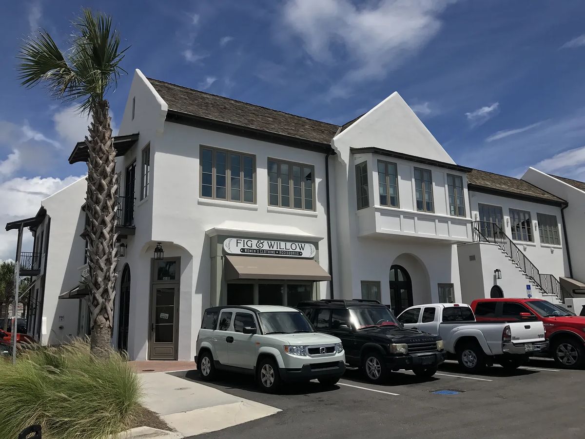 Exterior view of a two-story building with white stucco walls and large windows, featuring a 'FIG & WILLOW' sign.