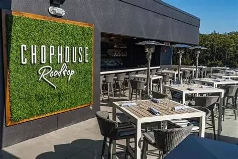 Outdoor deck area with white tables, gray wicker chairs, green wall sign, and patio heaters.