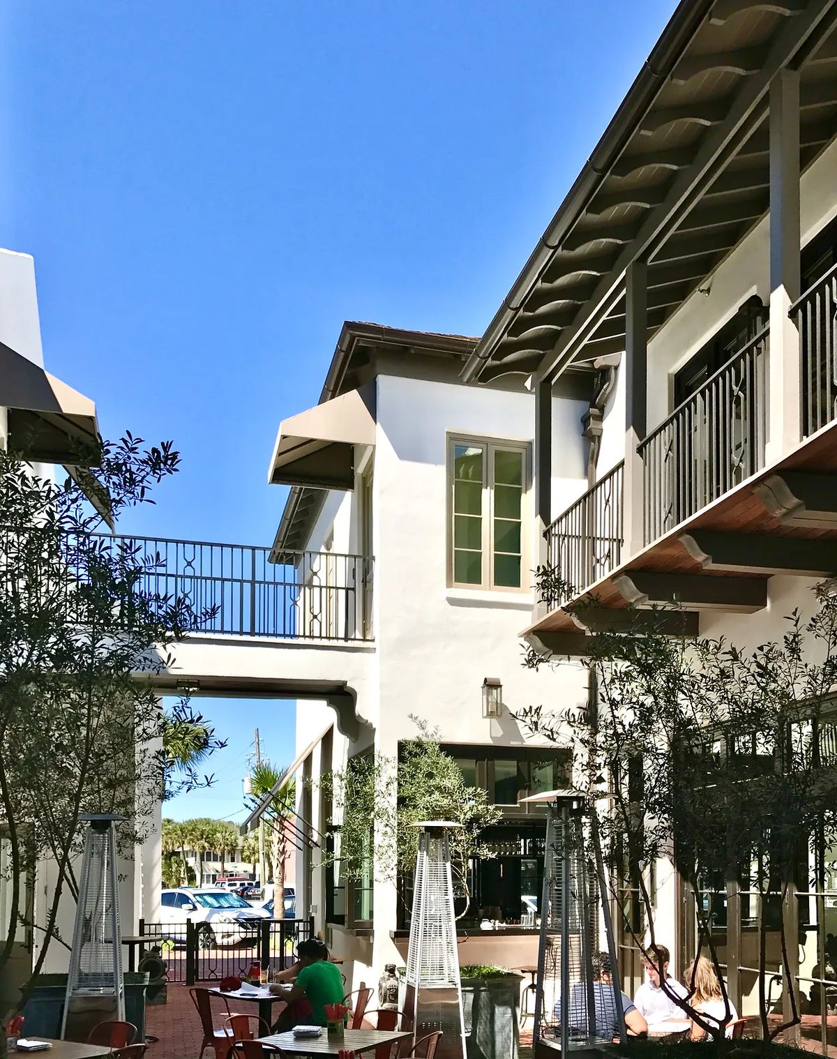 Exterior courtyard with tables, olive trees, balconies, and a connecting bridge between buildings.