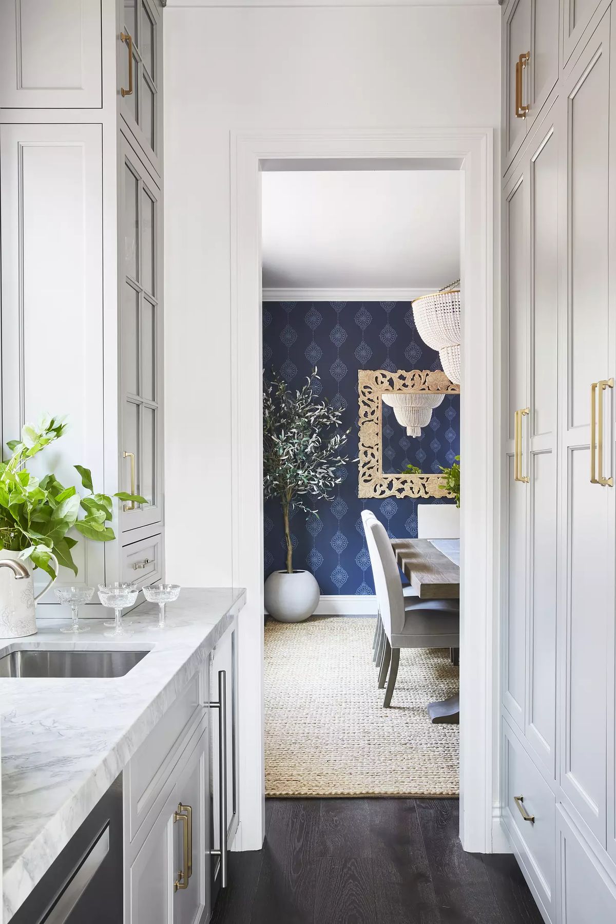 Kitchen with white cabinetry, marble countertop, sink, and doorway to a dining area with decorative elements
