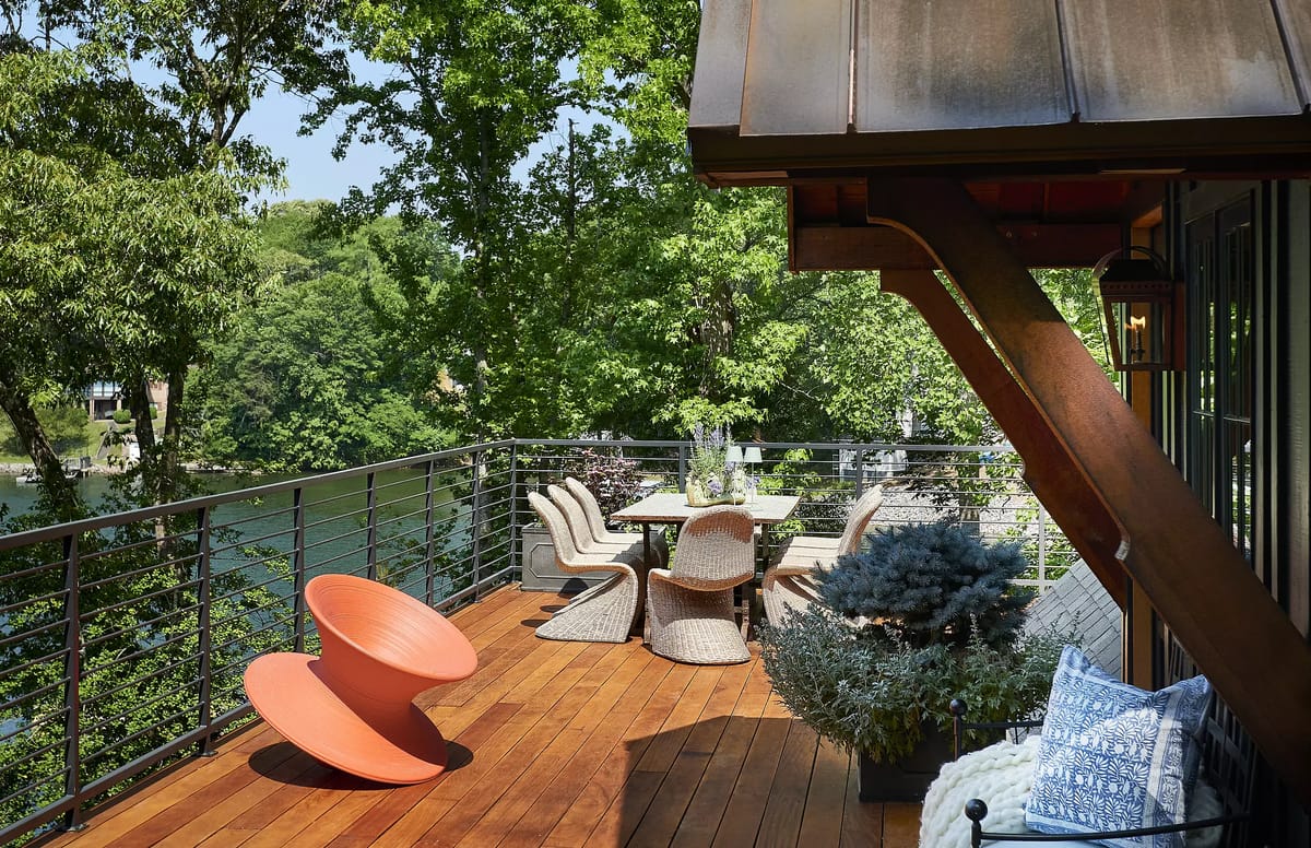 Deck with wooden floor, round orange chair, dining table with chairs, and potted plants overlooking water