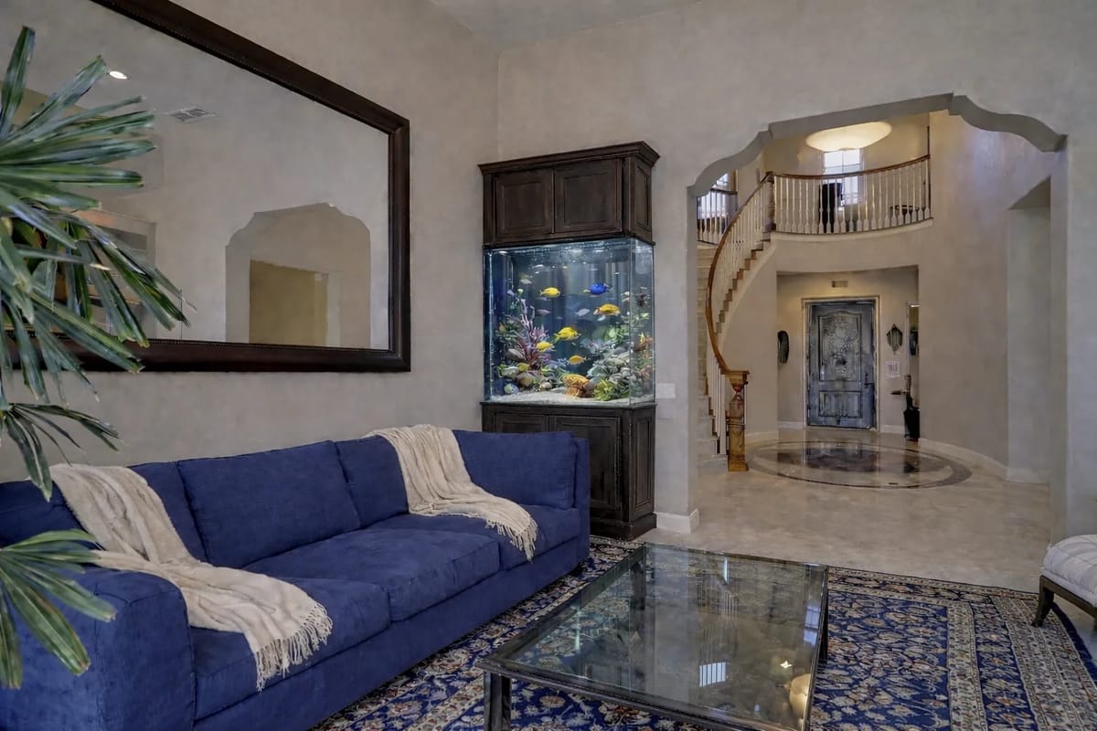 Foyer with blue sofa, glass coffee table, aquarium, staircase, and decorative rug.