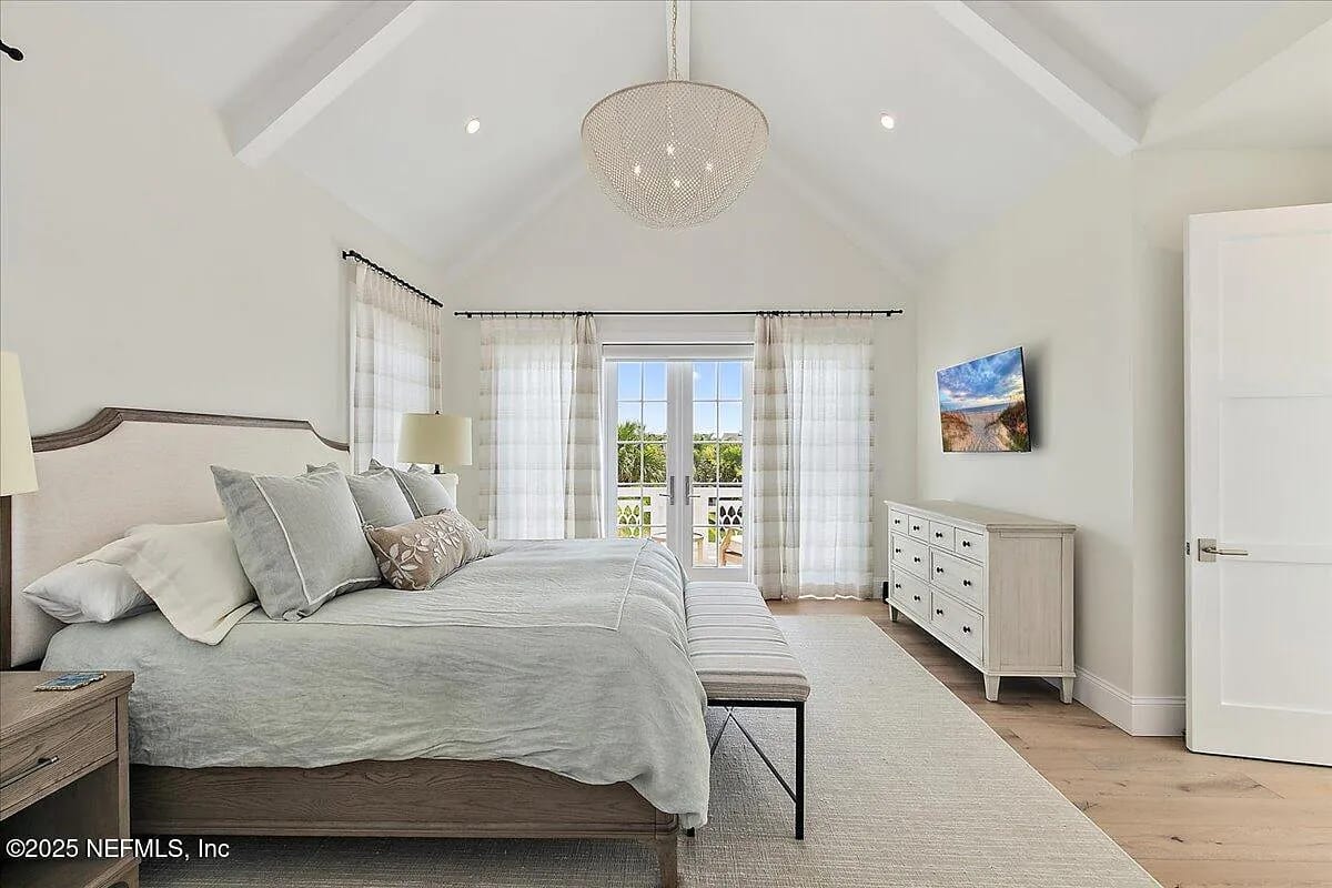 Bedroom with king-sized bed, nightstands, bench, dresser, large windows, and a mounted television.