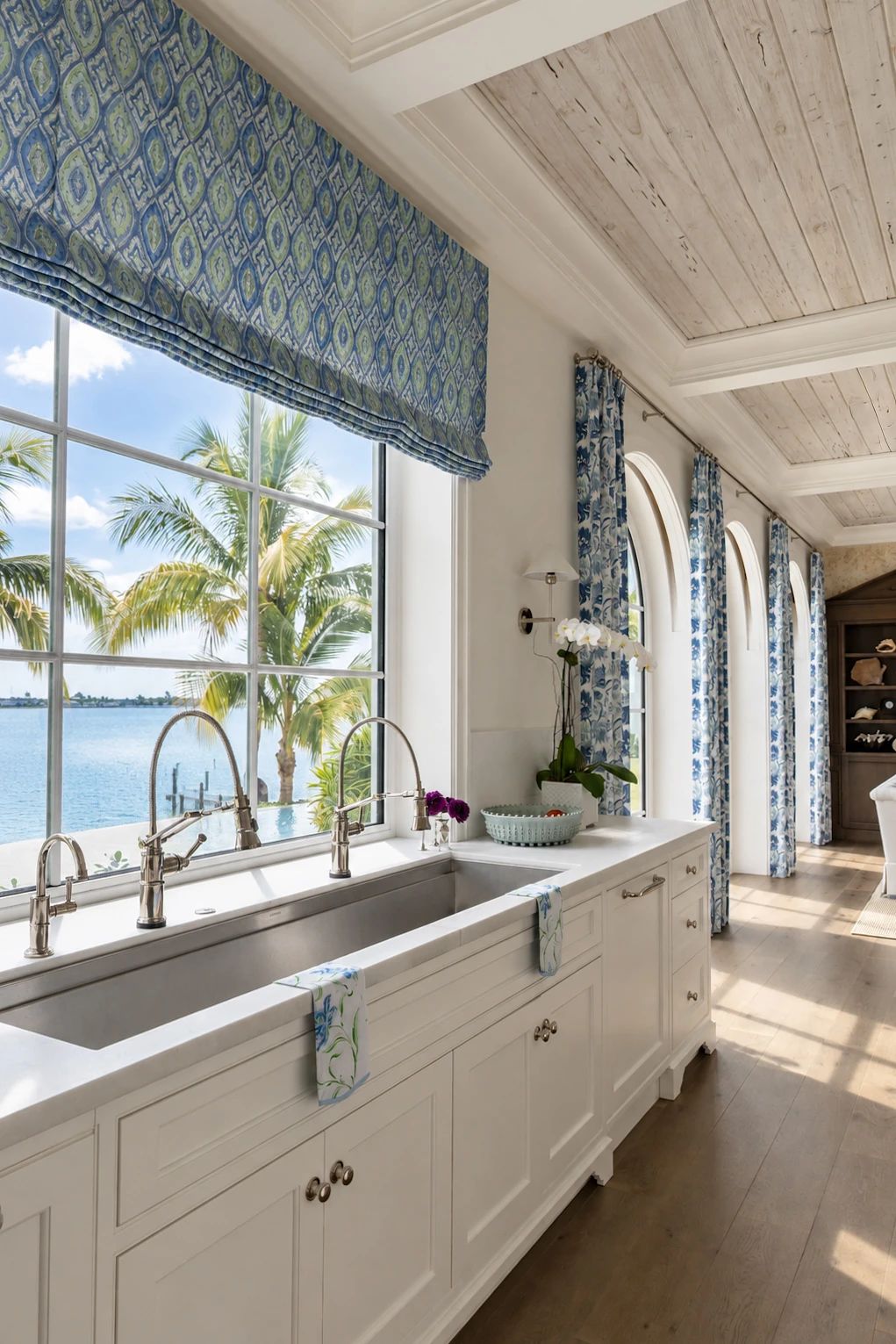 Kitchen with a double sink, white cabinetry, and large windows overlooking palm trees.