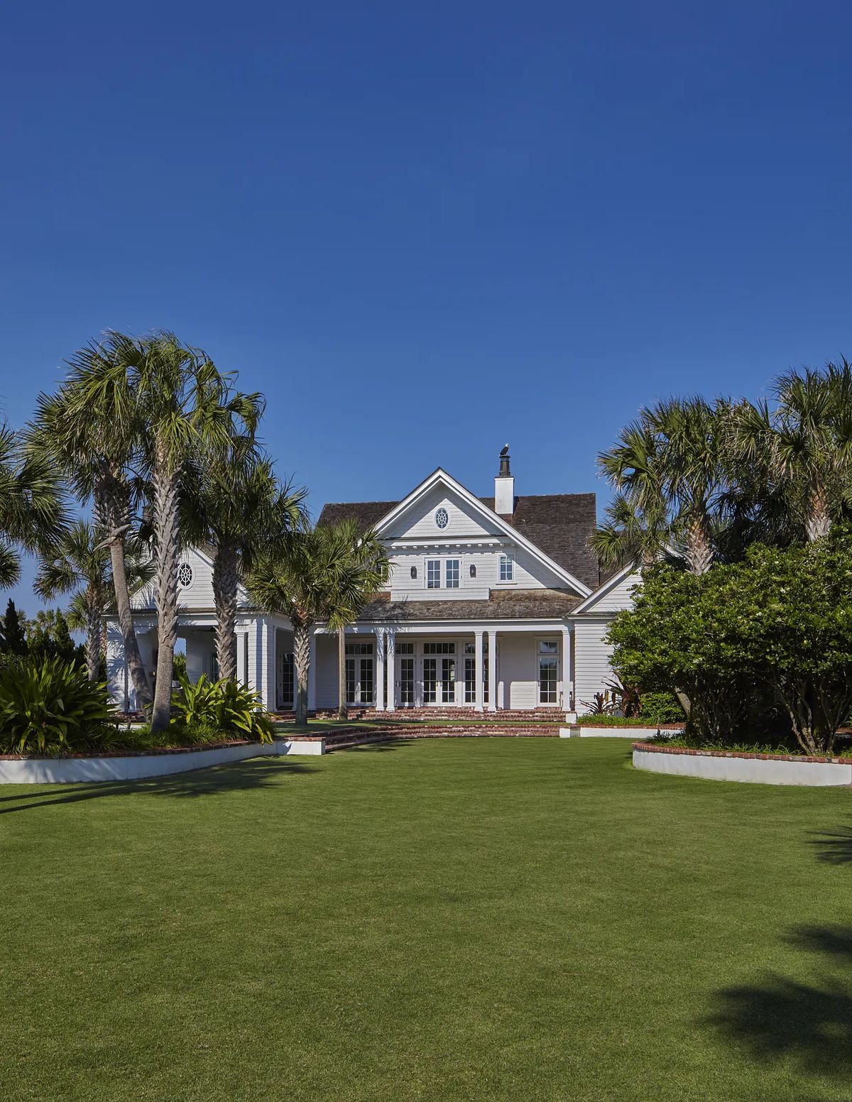 Front exterior view of a house with gabled roof, light gray siding, porch, and palm trees.