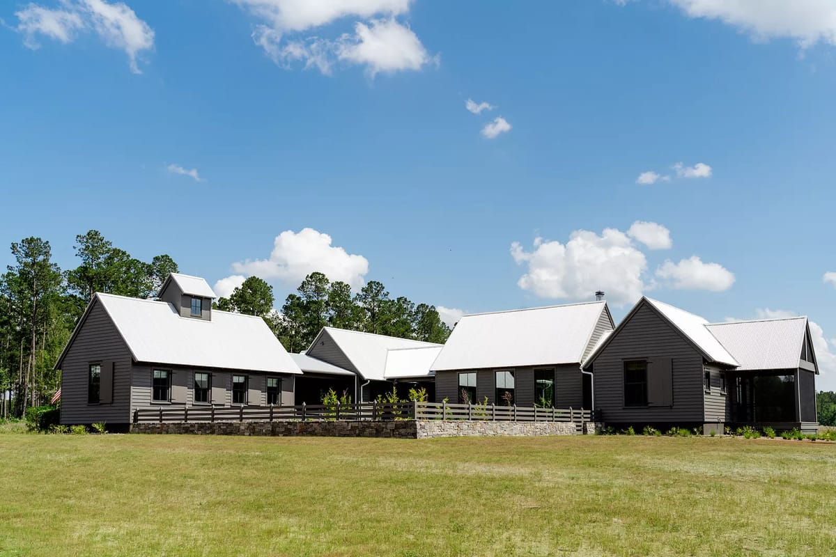 Exterior front view of a building with gabled roofs, dark wood siding, stone wall, and a wooden fence.