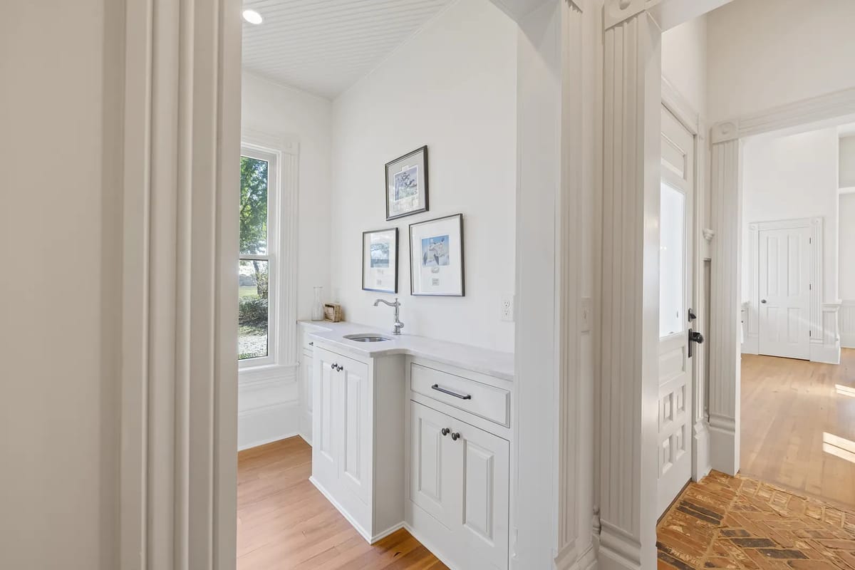Laundry room with white cabinet, sink, framed artwork, and window providing natural light.