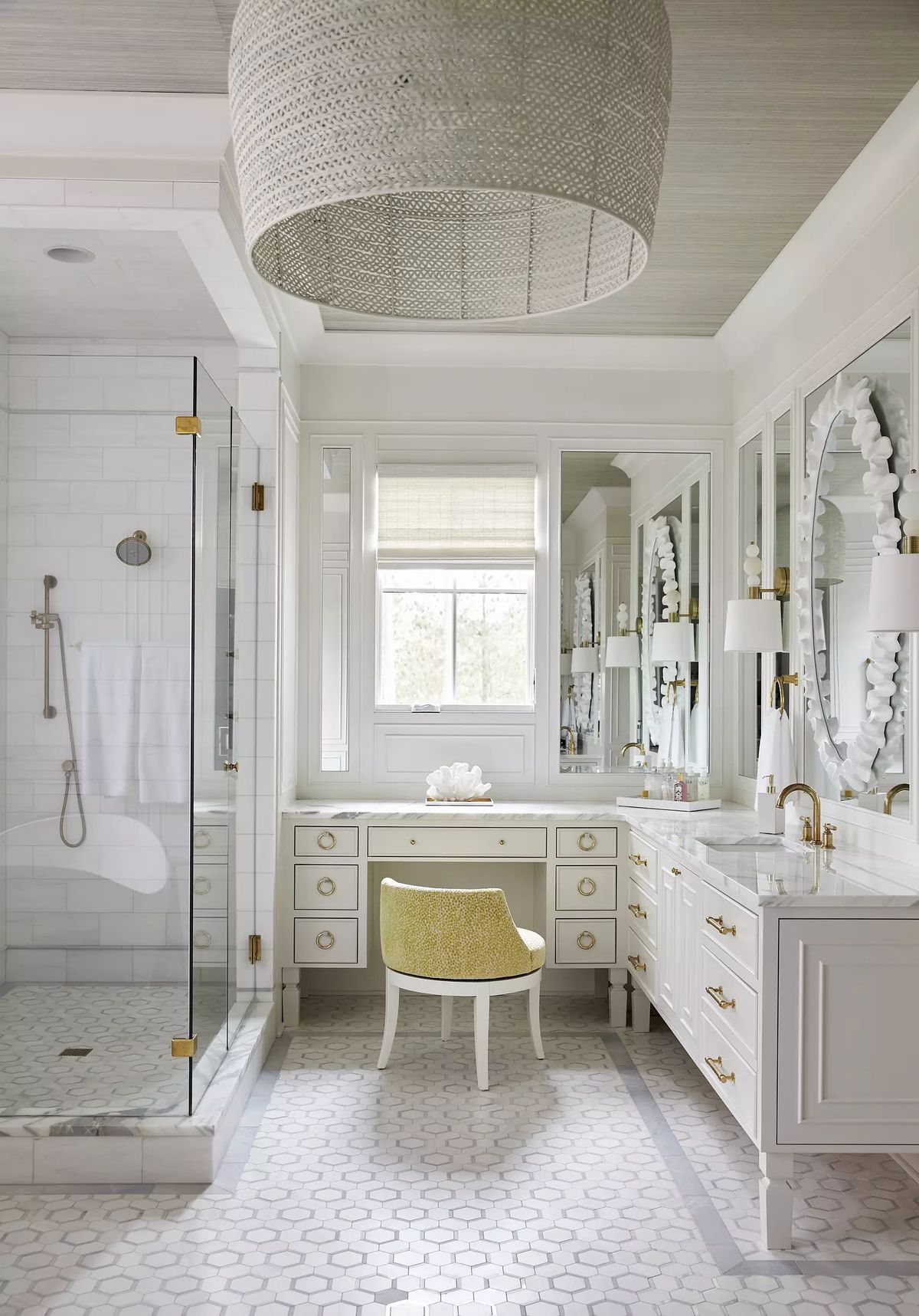 Bathroom with glass shower, double vanity, yellow chair, large mirror, hexagonal tiles, and woven ceiling light.