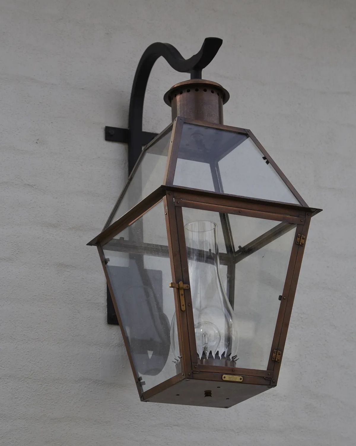Wall-mounted lantern with glass enclosure and metal frame featuring an ornate arm.