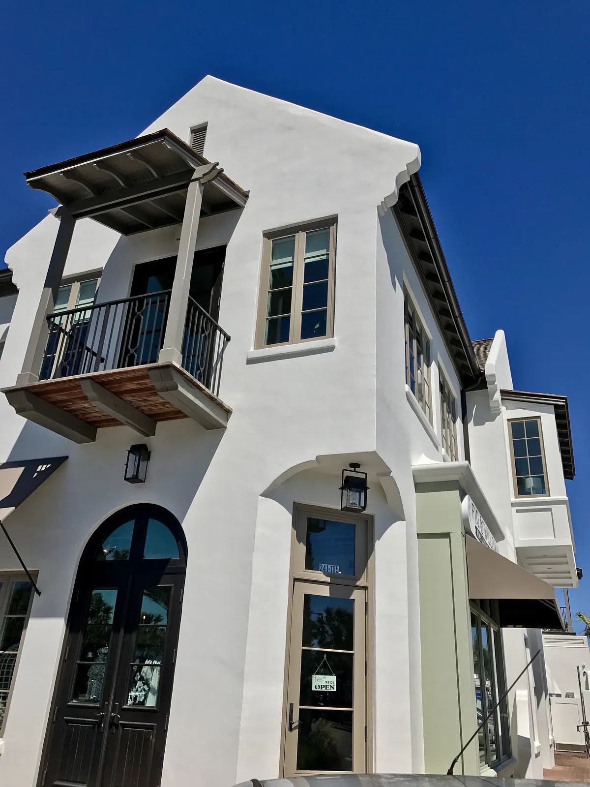 Exterior view of a building with white stucco, decorative elements, balcony, and multiple windows.