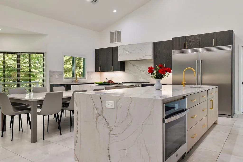 Kitchen with dark cabinetry, marble countertops, stainless steel appliances, and central island with seating.