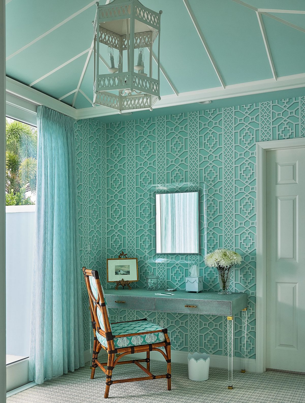Office with light blue patterned wall, desk, chair, mirror, and sheer curtains.