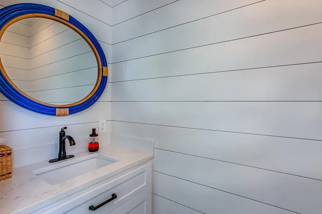 Powder room with white sink cabinet, blue-bordered mirror, and white shiplap walls.