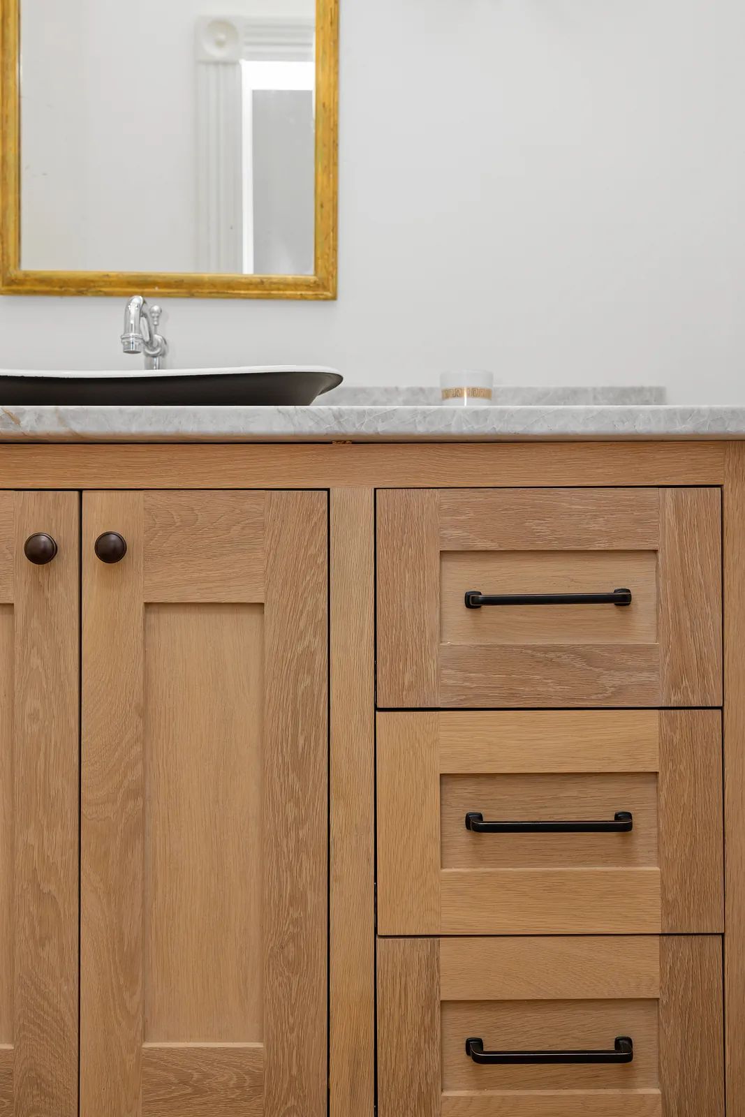 Bathroom with wooden vanity, marble countertop, sink, and gold-framed mirror.