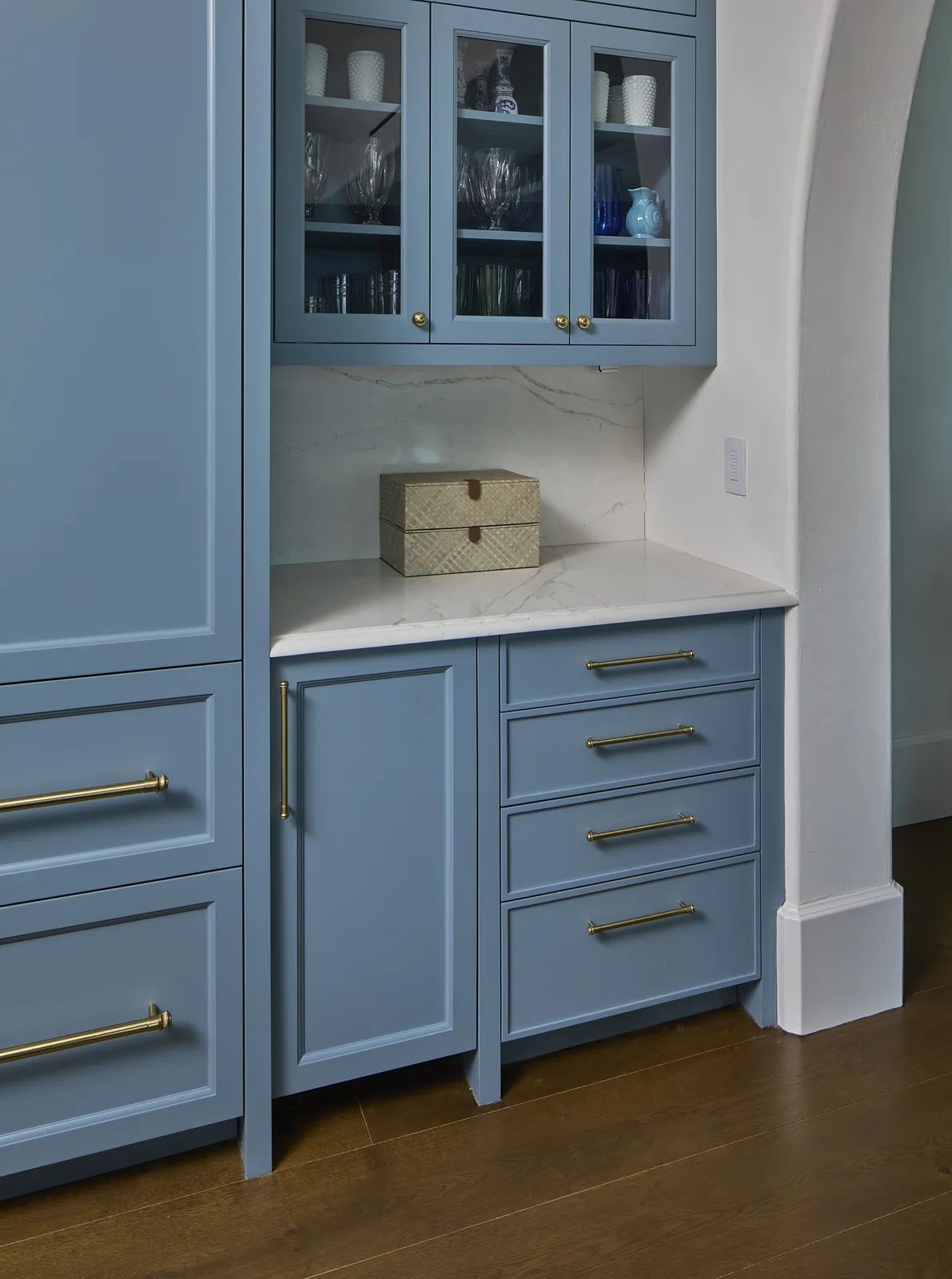 Kitchen with blue cabinetry, marble countertop, decorative box, and gold hardware.
