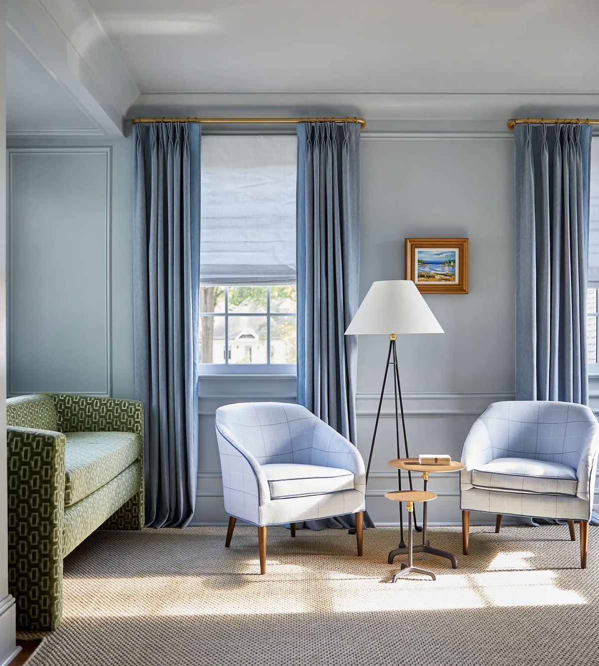 Living room with two armchairs, side table, green sofa, large windows, drapes, and framed artwork