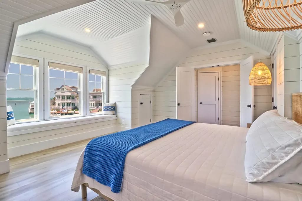 Bedroom with white bed, blue blanket, window seat, shiplap walls, and sloped ceiling