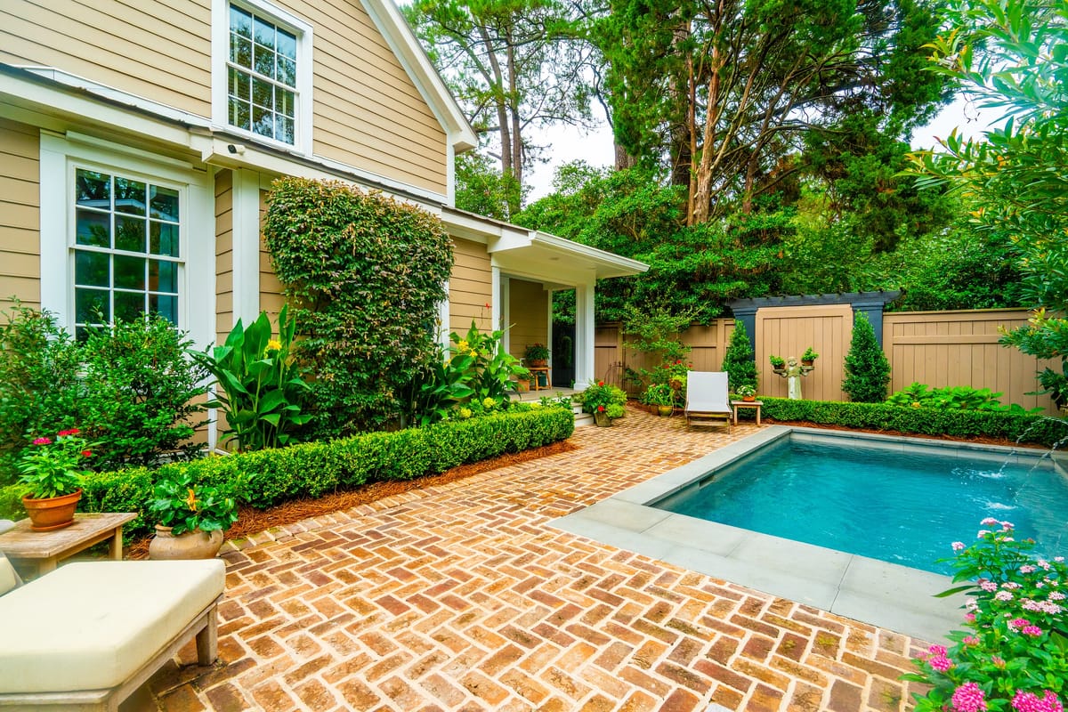 Patio with swimming pool, brick paving, lounge chair, and landscaped greenery.